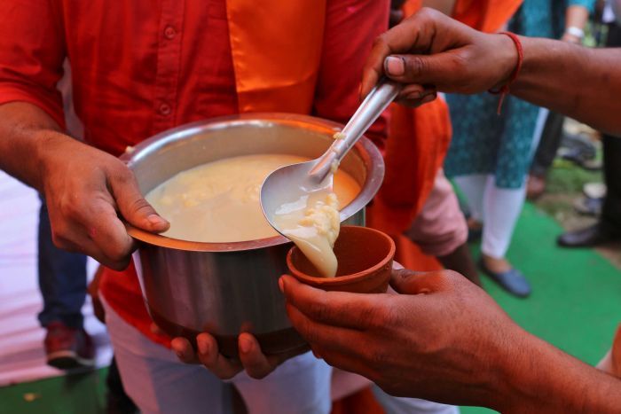 A man holds a pot filled with yellow curdled liquid as a man spoons some of it into a cup.