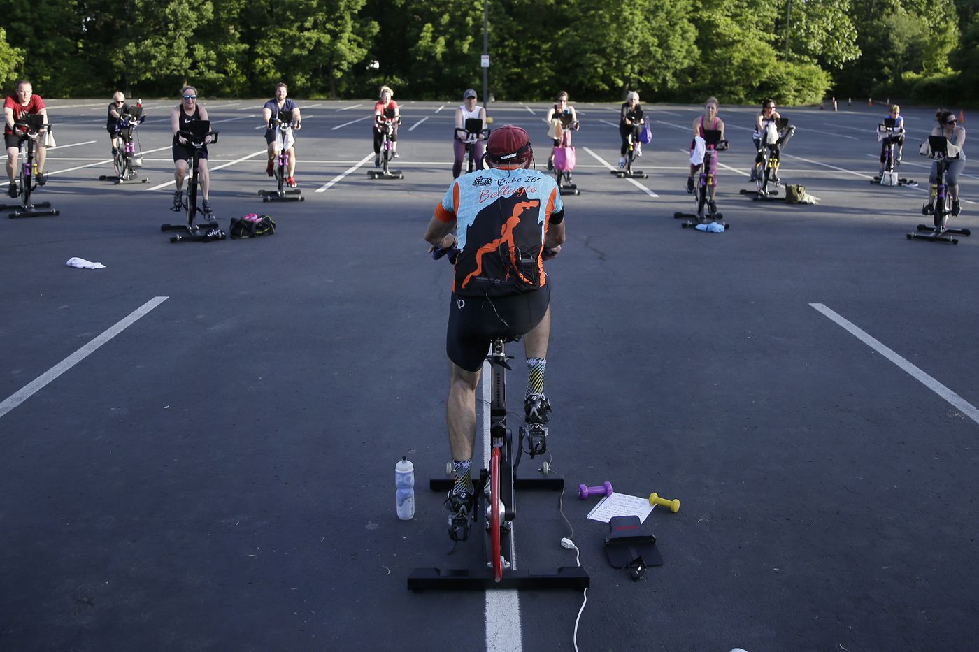 Cycling instructor Tom Hambrose (foreground) leads the 45 minute “Cycling with Tom” spin class in the parking lot at Royal Fitness in Barrington, N.J. on May 27, 2020. Gyms in New Jersey can hold outdoor classes, with restrictions, but indoor use has not been authorized yet.