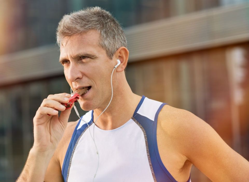 Older male runner eating protein bar