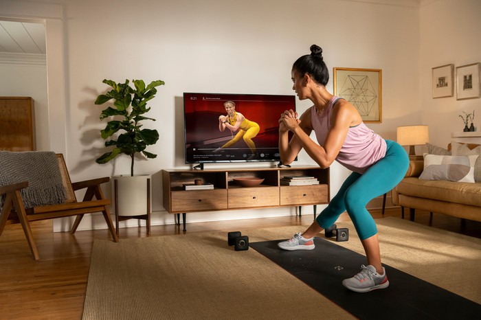 Woman on exercise mat in a living room following a Peloton workout on a TV