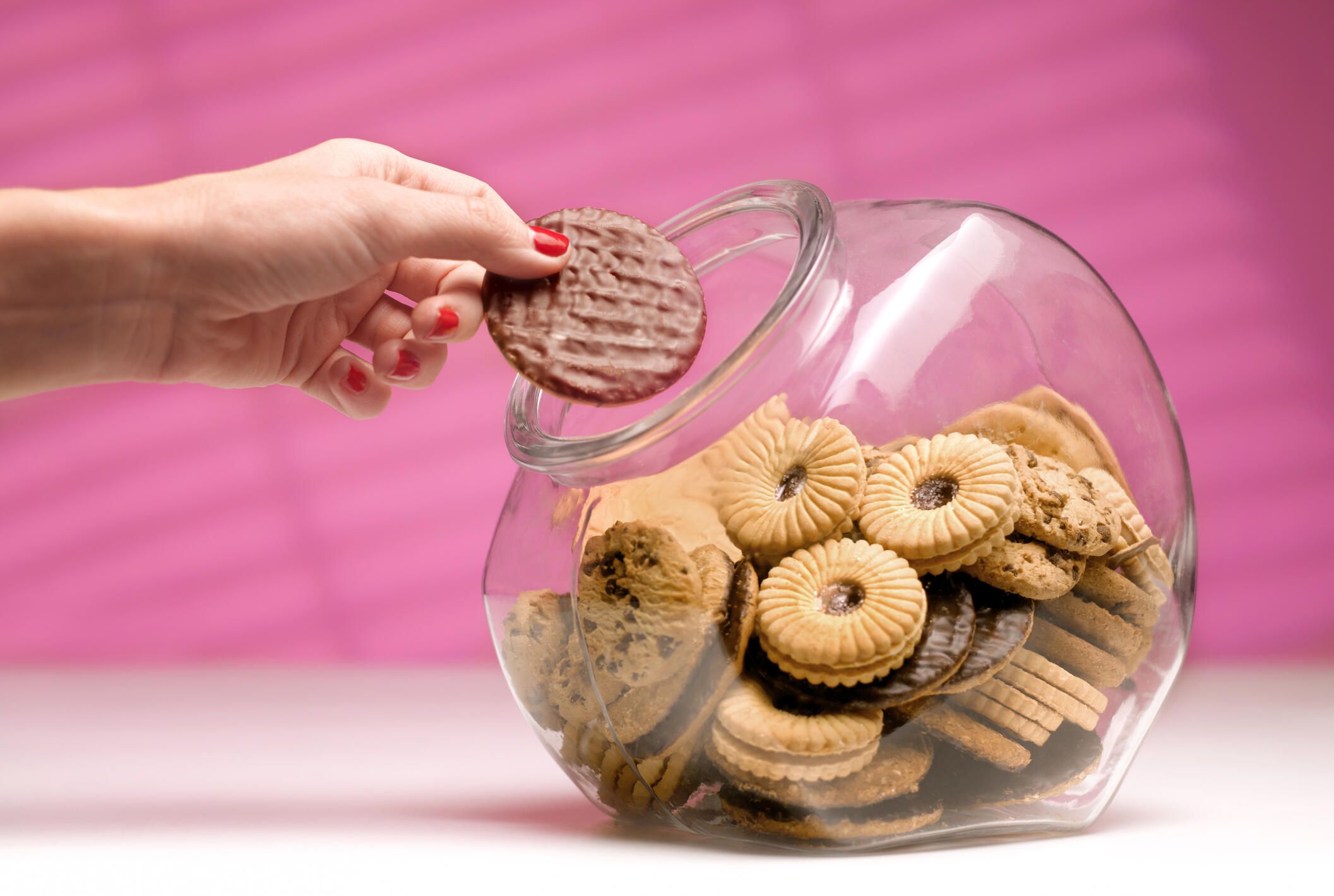 hand taking a cookie out of a cookie jar, pink background