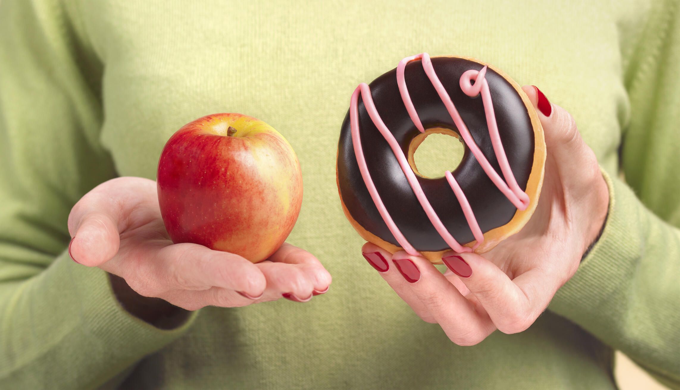 close-up of a woman holding an apple and a donut
